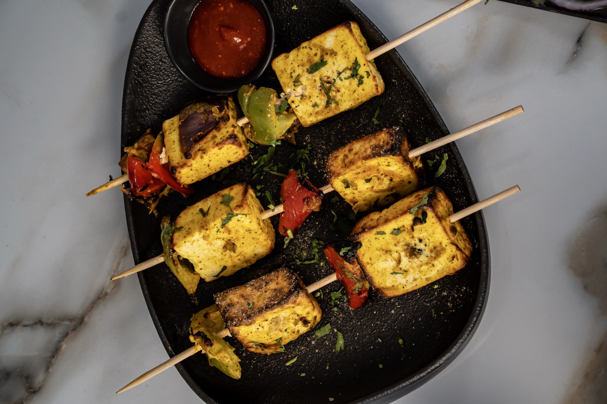 Paneer tikka skewers with charred peppers on black stoneware